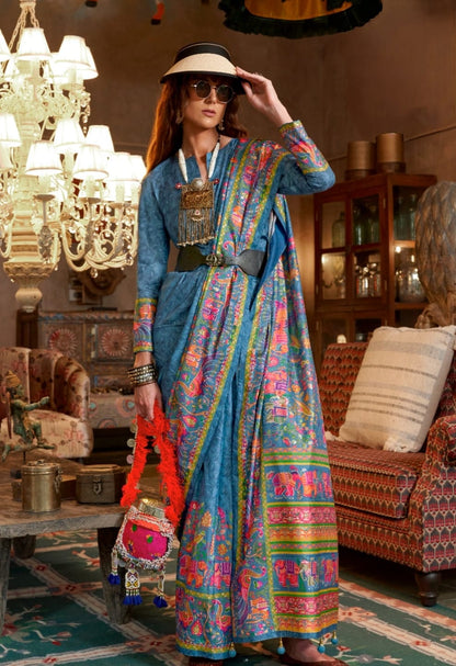 Woman in a colorful saree standing in an ornate room with chandeliers and furniture.